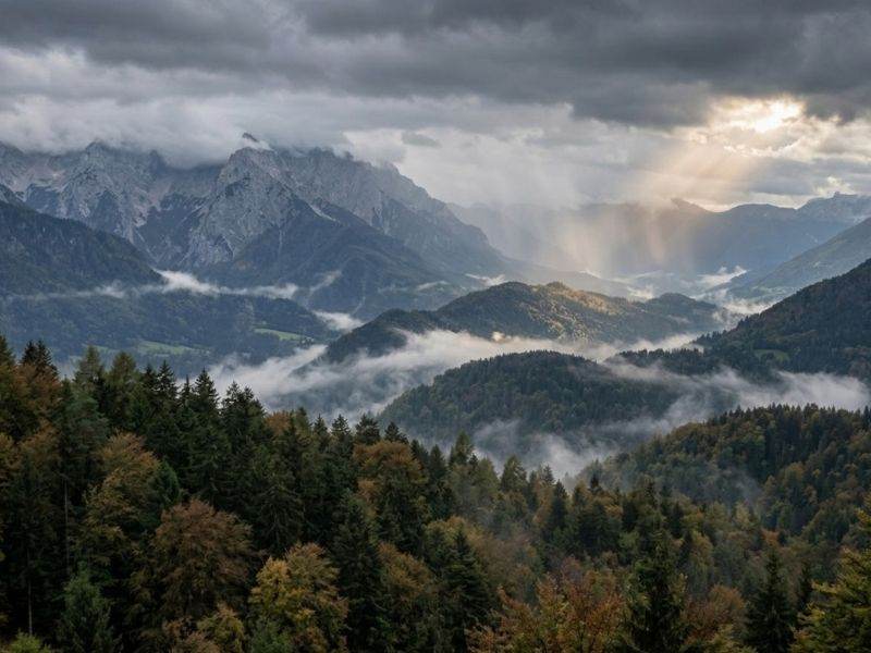 Deževni oblaki nad slovenskimi Alpami, meglice nad gozdovi in sončni žarki skozi oblake