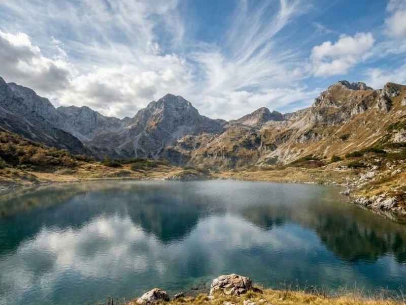 Jutranja meglica nad alpskim jezerom in koprenasta oblačnost nad gorami